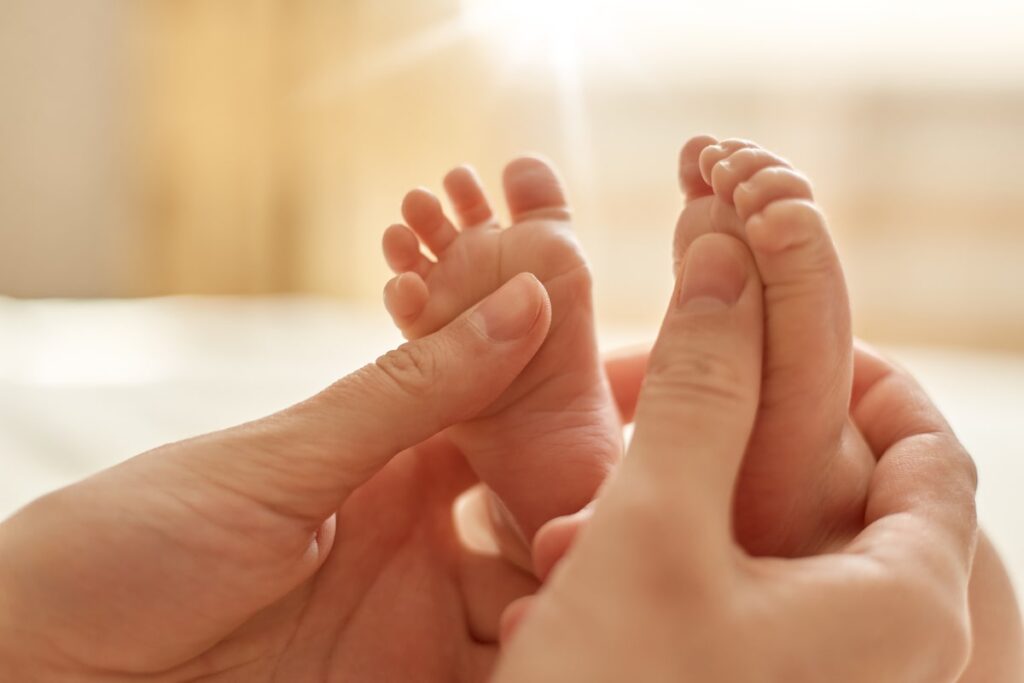 mum making baby massage mother massaging infant bare foot preventive massage newborn mommy stroking baby s feet with both hands light background min